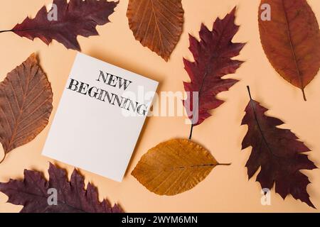 Ein weißes Stück Papier mit der Aufschrift „New Beginning“ wird auf einen Stapel Herbstblätter gelegt Stockfoto