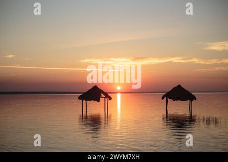 Ein wunderschöner Sonnenuntergang über dem See Peten Itza im Norden Guatemalas wirft orange rosa und blaue Farbtöne über das ruhige Wasser, mit Hütten im Wasser Stockfoto