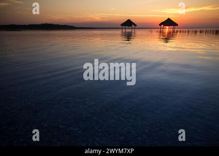 Ein wunderschöner Sonnenuntergang über dem See Peten Itza im Norden Guatemalas wirft orange rosa und blaue Farbtöne über das ruhige Wasser, mit Hütten im Wasser Stockfoto