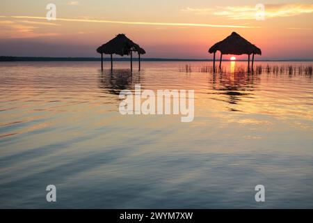 Ein wunderschöner Sonnenuntergang über dem See Peten Itza im Norden Guatemalas wirft orange rosa und blaue Farbtöne über das ruhige Wasser, mit Hütten im Wasser Stockfoto