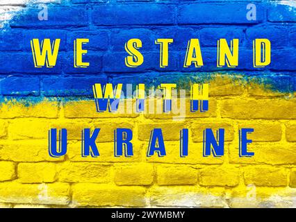 Eine blau-gelbe Wand mit den Worten „Wir stehen mit der Ukraine“. Die Farben der Wand und des Textes schaffen ein Gefühl der Einheit und Unterstützung für Stockfoto