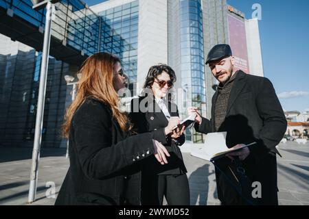 Drei junge Unternehmer führen in einem urbanen Umfeld mit Technologie und Notizblöcken eine Geschäftsdiskussion. Stockfoto