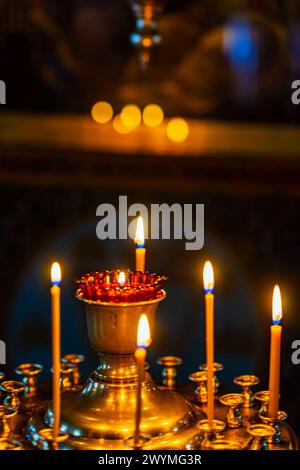 Das Licht der Kerzen, die in goldenen Kerzenleuchtern im Tempel brennen. Abstrakter vertikaler Hintergrund mit Bokeh, selektiver Fokus Stockfoto