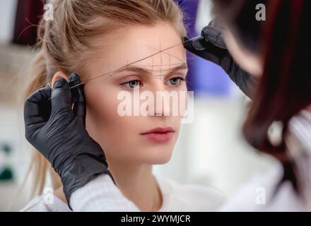 Permanent Tattoo Make-up Master definiert mit professionellen Werkzeugen die ideale Augenbrauenform. Nahaufnahme des Mikroblading-Arbeitsprozesses Stockfoto