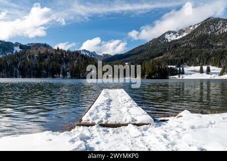 Die Seebrücke mit Schnee und menschlichen Fußspuren schafft an einem ruhigen Nachmittag am See im Alpental eine Urlaubsatmosphäre. Stockfoto
