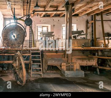 Das Innere der alten italienischen Wassermühle des Potals in der Provinz Cuneo, Italien. Hölzerne Mühlenkonstruktion mit großem Mühlstein Stockfoto