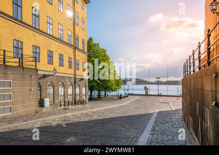 Warmes Sonnenlicht taucht die historischen Gebäude und kopfsteingepflasterten Straßen in Riddarholmen auf und überblickt die ruhige Uferpromenade, während der Tag in den Abend übergeht. Stockholm, Schweden Stockfoto