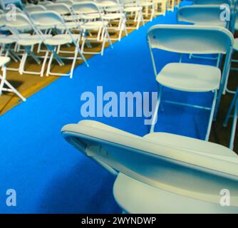 Weiße Klappstühle in Reihen mit blauem Läufer für eine Veranstaltung wie Hochzeit, Abschlussfeier, Bandschneiden, Jubiläum, Vortrag, usw. Hochwertige Fotos Stockfoto