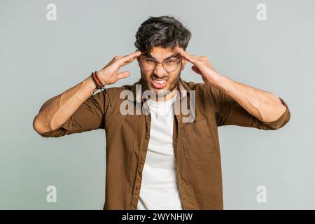 Unzufrieden erschöpfter indischer Hindu-Mann, der Schläfen reibt, um Kopfschmerzen zu heilen, leidet unter Spannung, Migräne, Stress, grimmigen Schmerzen, Bluthochdruck isoliert auf grauem Hintergrund Stockfoto