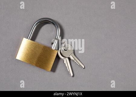 Vorhängeschloss aus Stahl mit Schlüsseln auf grauem Hintergrund, Draufsicht. Leerzeichen für Text Stockfoto