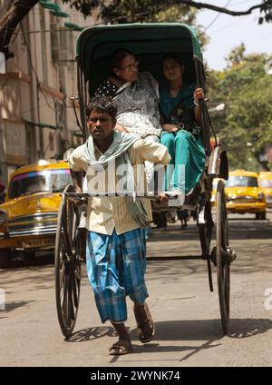 Kalkutta Rikscha Wallahs mit Passagieren. Kalkutta ist einer der einzigen Orte der Welt, an denen noch immer Flotten handgezogener Rikschas die Straßen befahren. Stockfoto