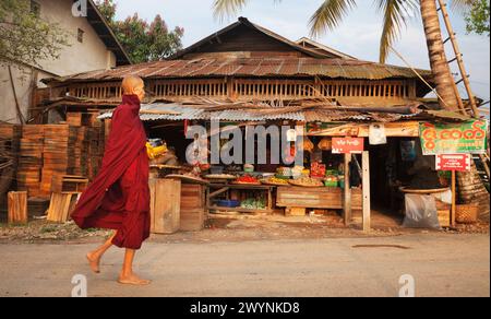 Buddhistischer Mönch in purpurrotem Gewand sammelt Almosen aus dem Laden in Hsipaw, Myanmar Stockfoto