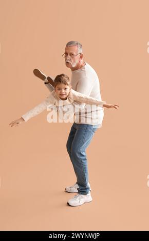 Großvater mit seinem glücklichen, süßen kleinen Enkel, der Spaß zusammen auf beigefarbenem Hintergrund hat Stockfoto