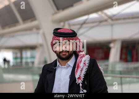 Vor dem Hintergrund einer schlanken, modernen Stadtlandschaft steht ein junger arabischer Geschäftsmann selbstbewusst, umgeben von Luxusautos und hohen Wolkenkratzern Stockfoto