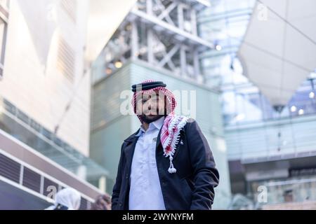Vor dem Hintergrund einer schlanken, modernen Stadtlandschaft steht ein junger arabischer Geschäftsmann selbstbewusst, umgeben von Luxusautos und hohen Wolkenkratzern Stockfoto