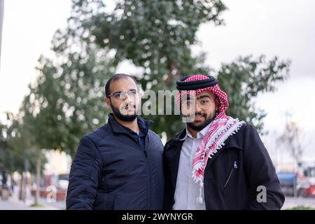 Vor dem Hintergrund einer schlanken, modernen Stadtlandschaft steht ein junger arabischer Geschäftsmann selbstbewusst, umgeben von Luxusautos und hohen Wolkenkratzern Stockfoto