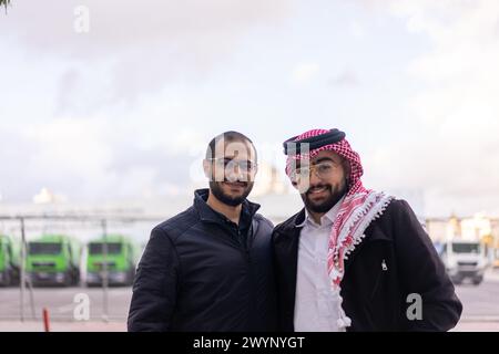 Vor dem Hintergrund einer schlanken, modernen Stadtlandschaft steht ein junger arabischer Geschäftsmann selbstbewusst, umgeben von Luxusautos und hohen Wolkenkratzern Stockfoto