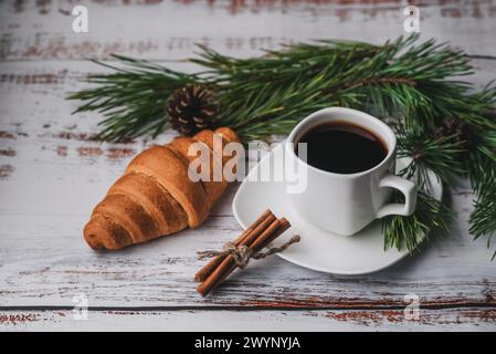 Eine Tasse Kaffee und ein Croissant mit Weihnachtsdekoration aus Tannenzweigen und Tannenzapfen Stockfoto