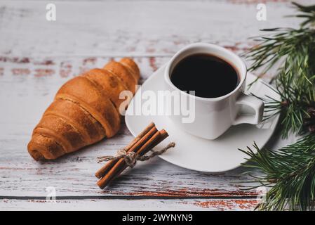 Eine Tasse Kaffee und ein Croissant mit Weihnachtsdekoration aus Tannenzweigen und Tannenzapfen Stockfoto