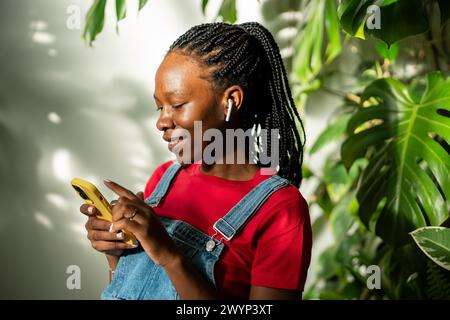 Entspannte schwarze Frau in Ohrhörern mit Smartphone zu Hause, wählt Lieblingstitel in der App aus. Stockfoto