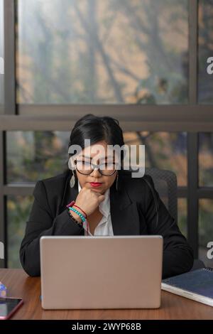 Geschäftsfrau, die ernsthaft auf den Laptop-Bildschirm schaut, während sie nachdenklich ist. Stockfoto