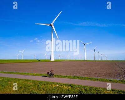 An einem sonnigen Tag im niederländischen Flevoland im Frühling fährt ein Mann mit seinem Elektrofahrrad eine Feldstraße entlang hoch aufragender Windturbinen. Männer auf dem Gelände des Elektrofahrrads Stockfoto