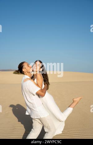 Vertikale Ansicht eines jungen Paares in weißem Outfit, das an einem sonnigen Tag am Strand Spaß hat Stockfoto