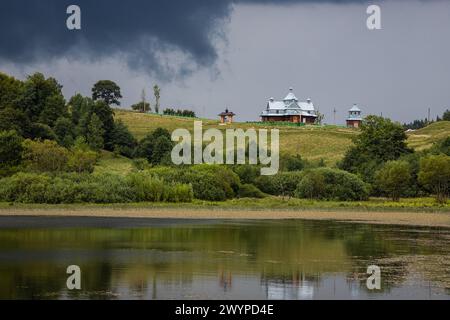 Sturmwolken, unheilvoller Himmel, Hügel und Kirche, grüne Bäume vor dem Regen. Stockfoto