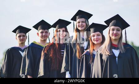 Fröhliche Absolventen posieren mit erhöhten Diplomen an einem sonnigen Tag. Stockfoto