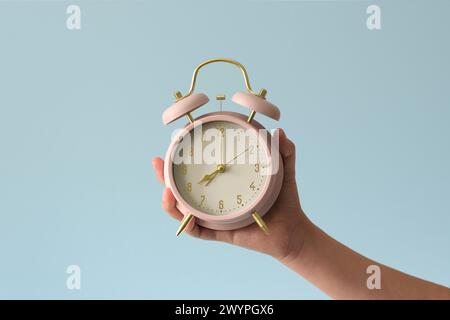 Ein Wecker in der Hand eines Kindes. Das Mädchen hält einen rosa mechanischen Wecker von gestern. Nahaufnahme. Hintergrund in sanften Blautönen Stockfoto