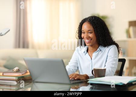 Glücklicher schwarzer Tele-Mitarbeiter, der zu Hause online mit einem Laptop arbeitet Stockfoto