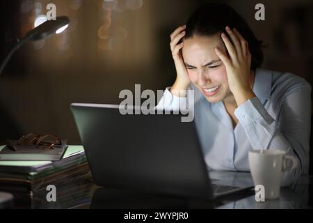 Verzweifelte Geschäftsfrau, die nachts im Homeoffice ihren Laptop überprüft Stockfoto