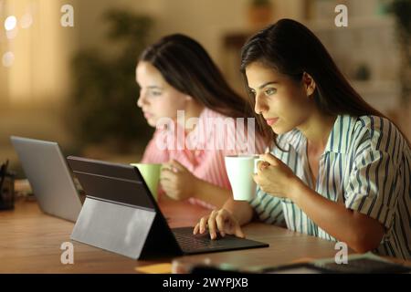 Zwei Telearbeiter trinken und arbeiten in der Nacht zu Hause online Stockfoto