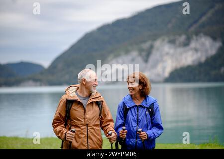 Porträt eines schönen aktiven älteren Ehepaares, das gemeinsam in den Frühlingsbergen wandert. Senioren stehen vor dem See. Stockfoto