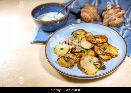 Knusprig gebratene Scheiben von Jerusalem Artischocke oder Topinambur (Helianthus tuberosus) mit Zwiebeln und Petersilie auf einem blauen Teller mit frischem Dip, gesunde Wurzel Stockfoto