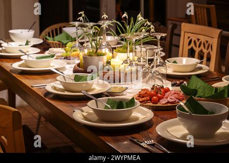 Dinnerparty für Familie und Freunde auf einem großen Holztisch mit verschiedenen Vintage Stühlen, festliche Atmosphäre mit Geschirr, Weingläsern und Dekoration, d Stockfoto