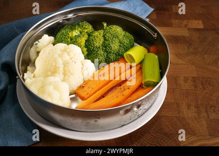 Gemüse wie Karotten, Brokkoli und Blumenkohl in einem Metallkorb auf einem dunklen rustikalen Holztisch, Kochmethode zum Konservieren von Vitaminen Stockfoto