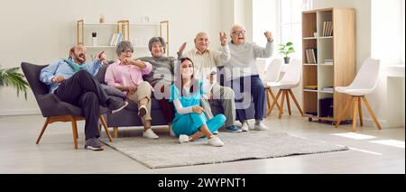 Gruppe von Senioren, die zusammen mit einer jungen Krankenschwester im Altersheim fernschauen. Stockfoto