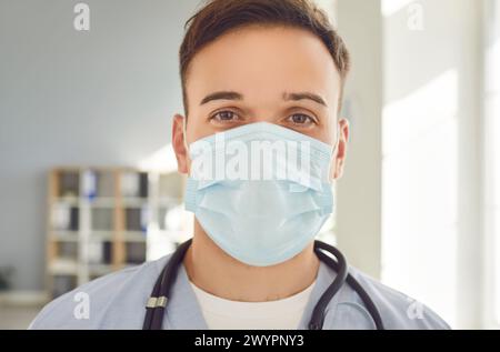 Junger Mann Arzt mit medizinischer Maske mit Stethoskop, der in der Klinik in die Kamera blickt. Stockfoto