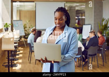 Porträt einer afroamerikanischen Frau, die im Büro steht und auf den Bildschirm eines Laptops blickt. Stockfoto