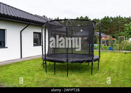 Großes Kinderspringtrampolin mit Schutznetz und geschlossenem Reißverschluss, im Garten stehend. Stockfoto