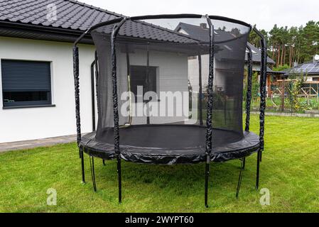 Großes Kinderspringtrampolin mit Schutznetz und geschlossenem Reißverschluss, im Garten stehend. Stockfoto