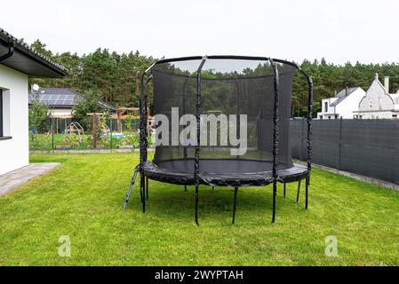 Großes Springtrampolin für Kinder mit Schutznetz und geschlossenem Reißverschluss, im Garten stehend, sichtbares Netz, das den Zaun bedeckt. Stockfoto