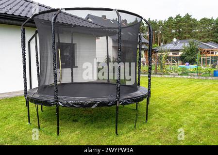 Großes Kinderspringtrampolin mit Schutznetz und geschlossenem Reißverschluss, im Garten stehend. Stockfoto