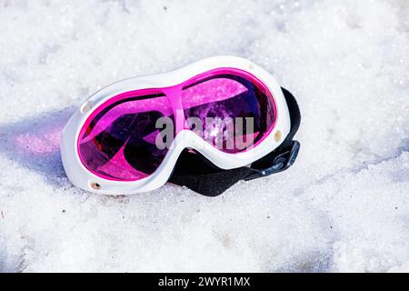 Die pinkfarbene Liegemaske liegt an einem sonnigen Tag auf einem nassen, schneebedeckten Hang. Winterschneesaison. Aktivurlaub mit Familie Stockfoto