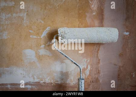 Malerwalze ausziehbarer Stab über rauer alter Betonwand während der Hausrenovierung in england großbritannien. Stockfoto