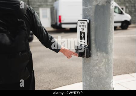 Nahaufnahme eines Mannes, der auf einer befahrenen Straße den Crosswalk-Knopf drückt Stockfoto