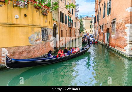 Traditionelle touristische Bootsausflüge: Gondelbootfahrten auf typischen Gondeln mit Gondoliern auf einem befahrenen schmalen Kanal in der Castello-Gegend von Venedig, Italien Stockfoto