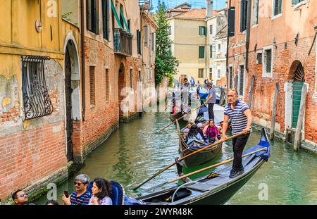 Traditionelle touristische Bootsausflüge: Gondelbootfahrten auf typischen Gondeln mit Gondoliern auf einem befahrenen schmalen Kanal in der Castello-Gegend von Venedig, Italien Stockfoto