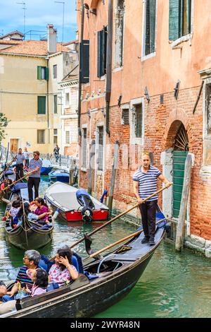 Traditionelle touristische Bootsausflüge: Gondelbootfahrten auf typischen Gondeln mit Gondoliern auf einem befahrenen schmalen Kanal in der Castello-Gegend von Venedig, Italien Stockfoto